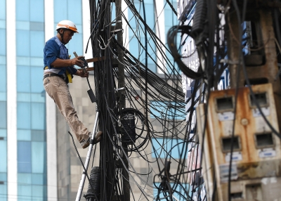 A Telecom company worker fixes cables atop a high pole in Hanoi