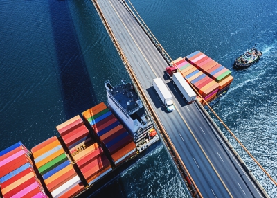 A boat carrying shipping containers passing underneath a bridge.