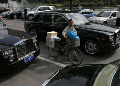 A man pushes his bicycle between Rolls-Royce Phantoms in a street in Shanghai, China